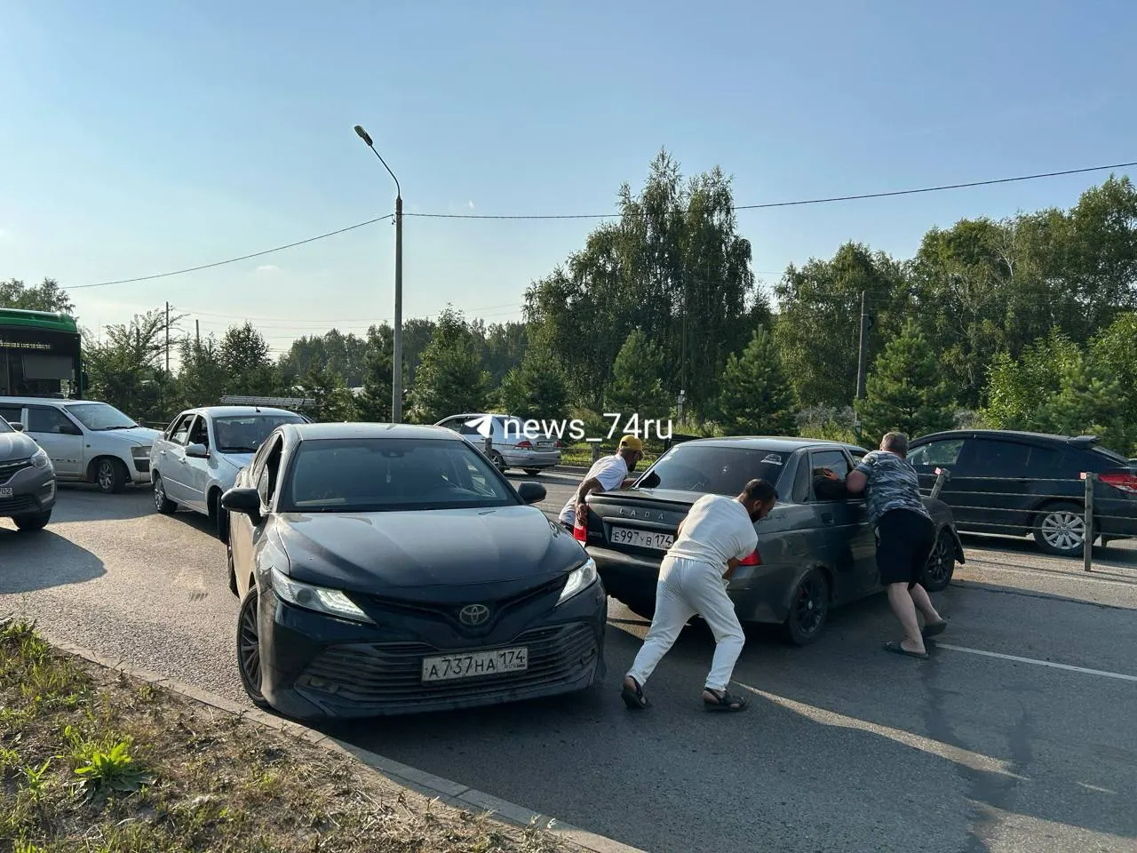 На выезде из района Западный произошла мелкая авария, из‑за которой образовалась большая пробка; водители пытаются оттолкать машину под палящим солнцем.